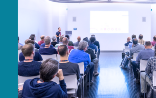 Zaal met mensen die naar een scherm kijken waar een presentatie wordt gegeven.