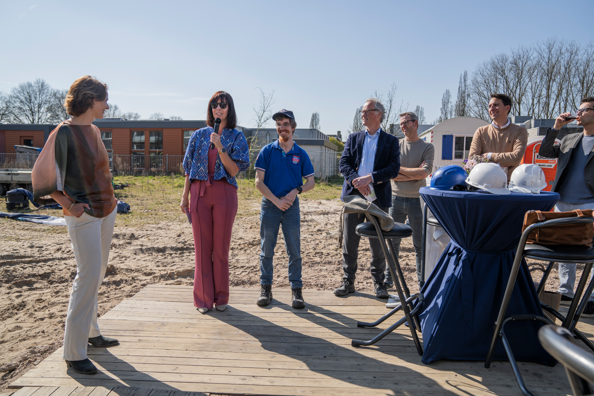 Bestuurder Marian van Heerebeek (RCS) spreekt de aanwezigen toe tijdens de feestelijke start van de bouw aan de Hertoglaan. Naast haar staat cliënt en lid van de centrale cliëntenraad Marius, en op de achtergrond luisteren genodigden mee.