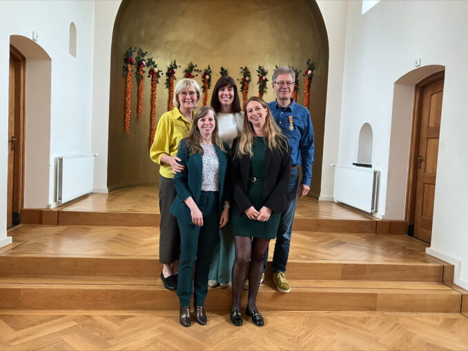 Peter_lintje_RCS Peter staat samen zijn vrouw en drie vrouwelijke collega’s op een houten podium voor een gouden wand met bloemendecoratie. Hij draagt zichtbaar trots zijn koninklijke onderscheiding op de borst.