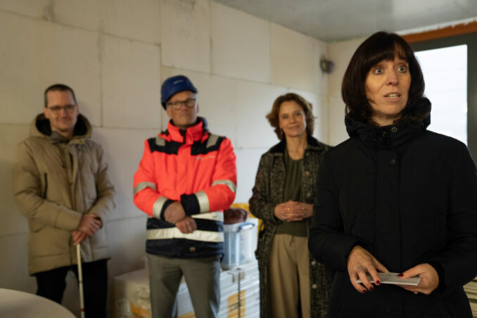 Wethouder Yvonne Vos bedient de machine voor de bronboring, waarmee zij officieel het startsein geeft voor de bouw. Omstanders kijken toe en applaudisseren.