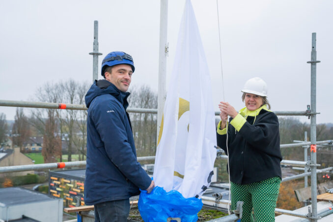 Wethouder Yvonne Vos bedient de machine voor de bronboring, waarmee zij officieel het startsein geeft voor de bouw. Omstanders kijken toe en applaudisseren.