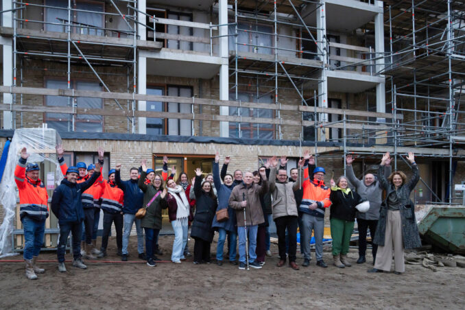 Bestuurder Marian van Heerebeek (RCS) spreekt de aanwezigen toe tijdens de feestelijke start van de bouw aan de Hertoglaan. Op de achtergrond luisteren genodigden mee.