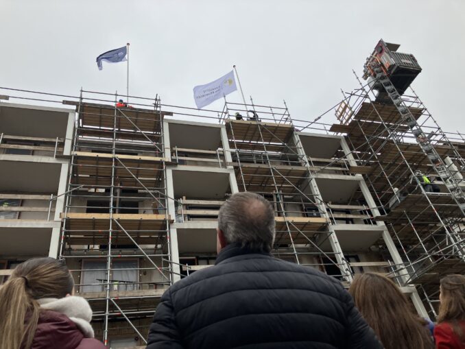Bestuurder Marian van Heerebeek (RCS) spreekt de aanwezigen toe tijdens de feestelijke start van de bouw aan de Hertoglaan. Op de achtergrond luisteren genodigden mee.
