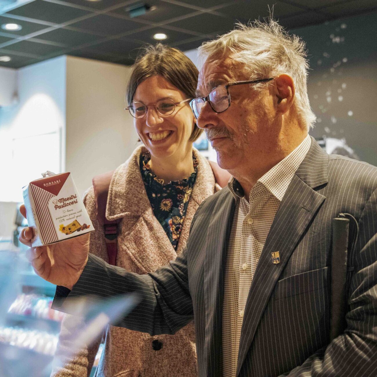 AWB 7 Een man houdt een product vast en bekijkt het, terwijl een begeleider naast hem staat en glimlacht.