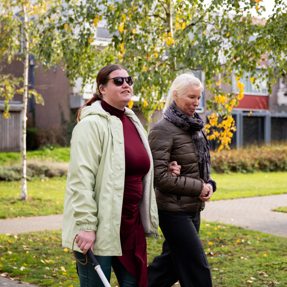 Een begeleider en een cliënt wandelen samen over een pad in een groene woonomgeving.