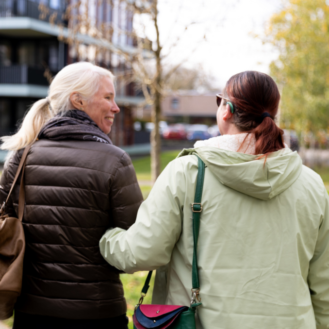 Website – wandelend van achter – 1000×1000 Een begeleider en een cliënt wandelen samen buiten en zijn met elkaar in gesprek.